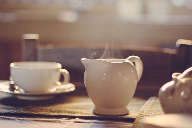 a white teapot sits on a breakfast table. Steam slowly rises.