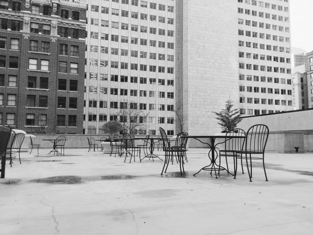 Empty cafe tables and chairs sit in a deserted courtyard surrounded by high-rise buildings.