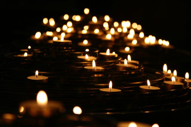 Many small candles burn in the darkness, as though at a vigil.