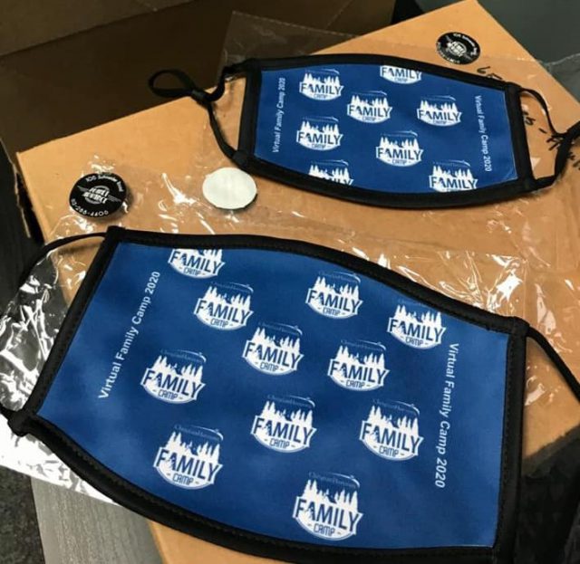 Two blue fabric COVID-19 masks lay on a cardboard box. The masks have the Christian Horizons Family Camp logo printed on them.