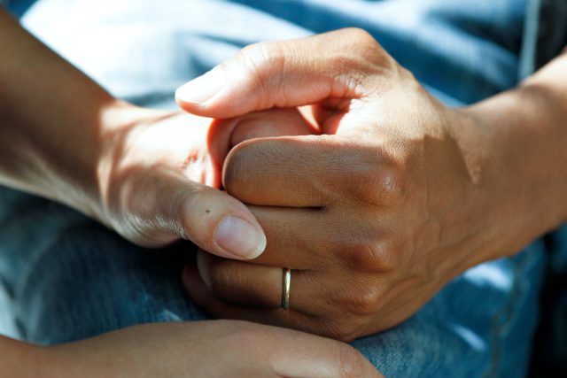 A closeup photo of two people holding hands. One has light skin (white) and one has skin that is a bit darker (brown).
