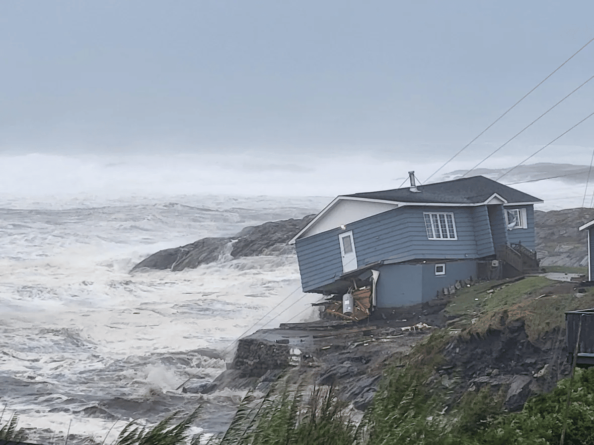 a blue house is being swept off a cliff by the raging ocean in the midst of a storm.